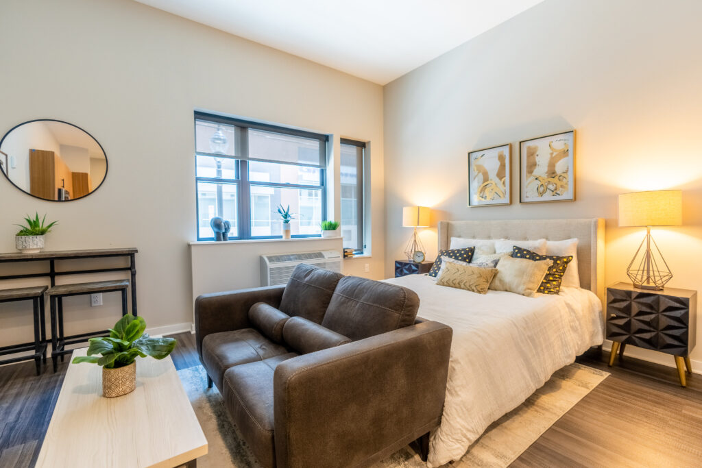 Bedroom and living room area with large windows in a studio apartment at The Hive.