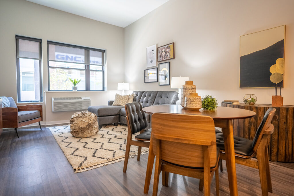 A living room with two large windows and hardwood-style flooring leading into a dining room area.