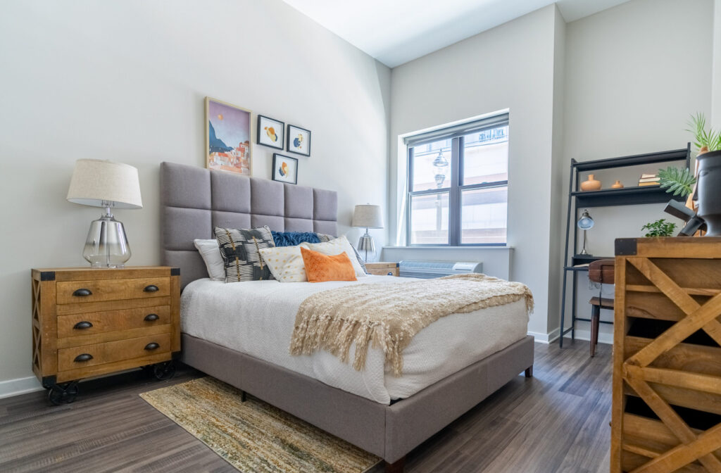Furnished bedroom with a window, white walls, and wooden floors at The Hive in Allentown, PA.