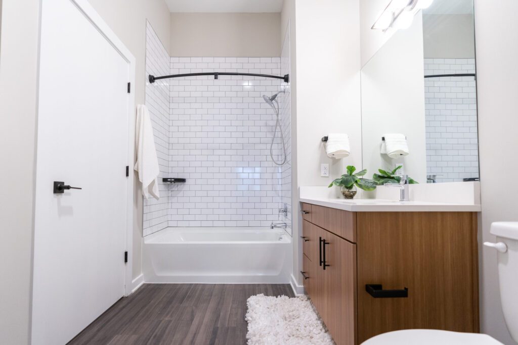 A bathroom with hardwood-style flooring, a large vanity, and a bathtub shower combo with subway tile.