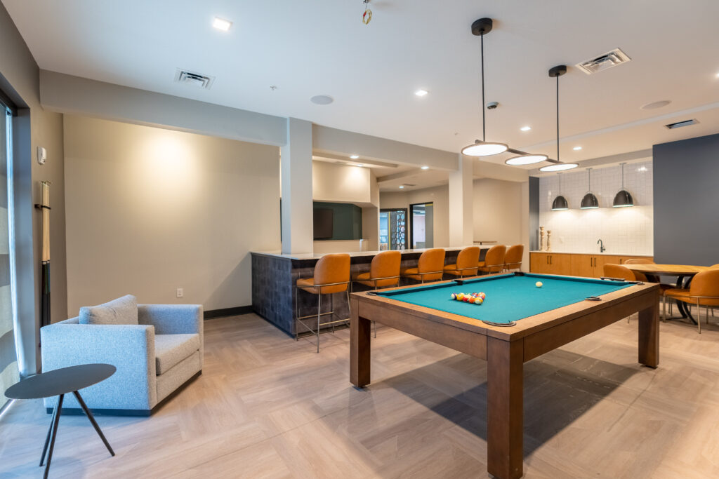 The Hive apartment's clubroom with a pool table, wet bar, bar seating, and a TV.
